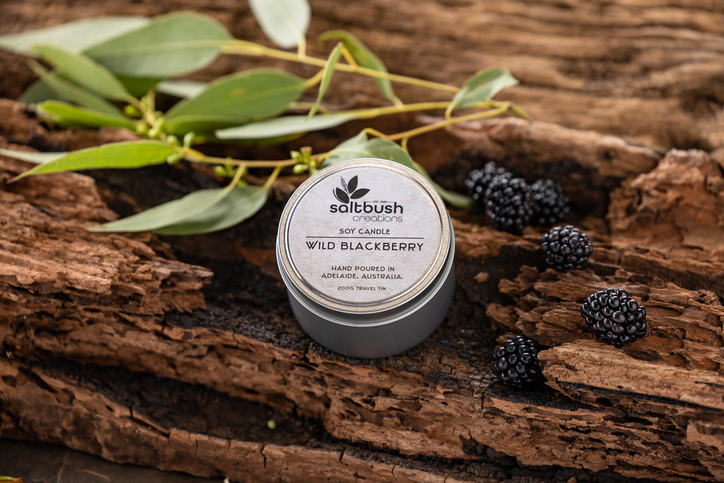 Wild blackberry candle sits on wooden log surrounded by blackberries 